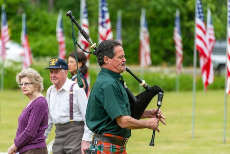 A kilted bagpiper performs outdoors at a Scottish festival with American flags in the background