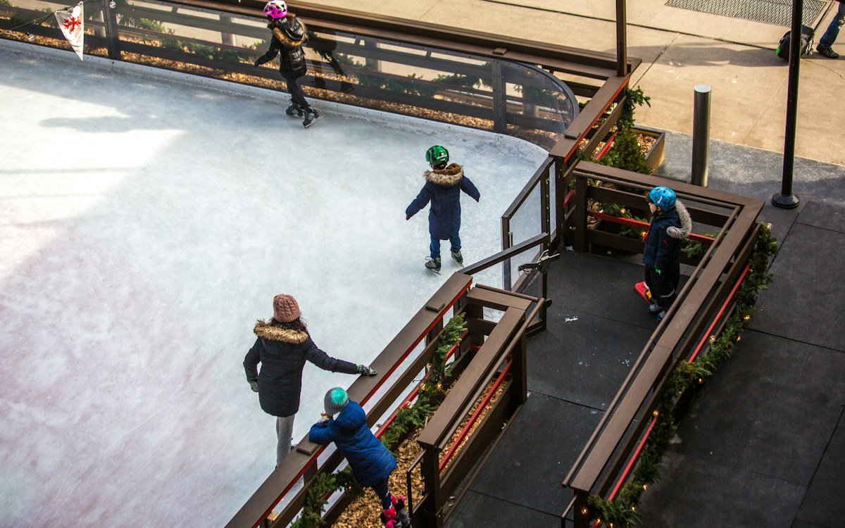 Children skating on an ice rink with a garland-trimmed railing