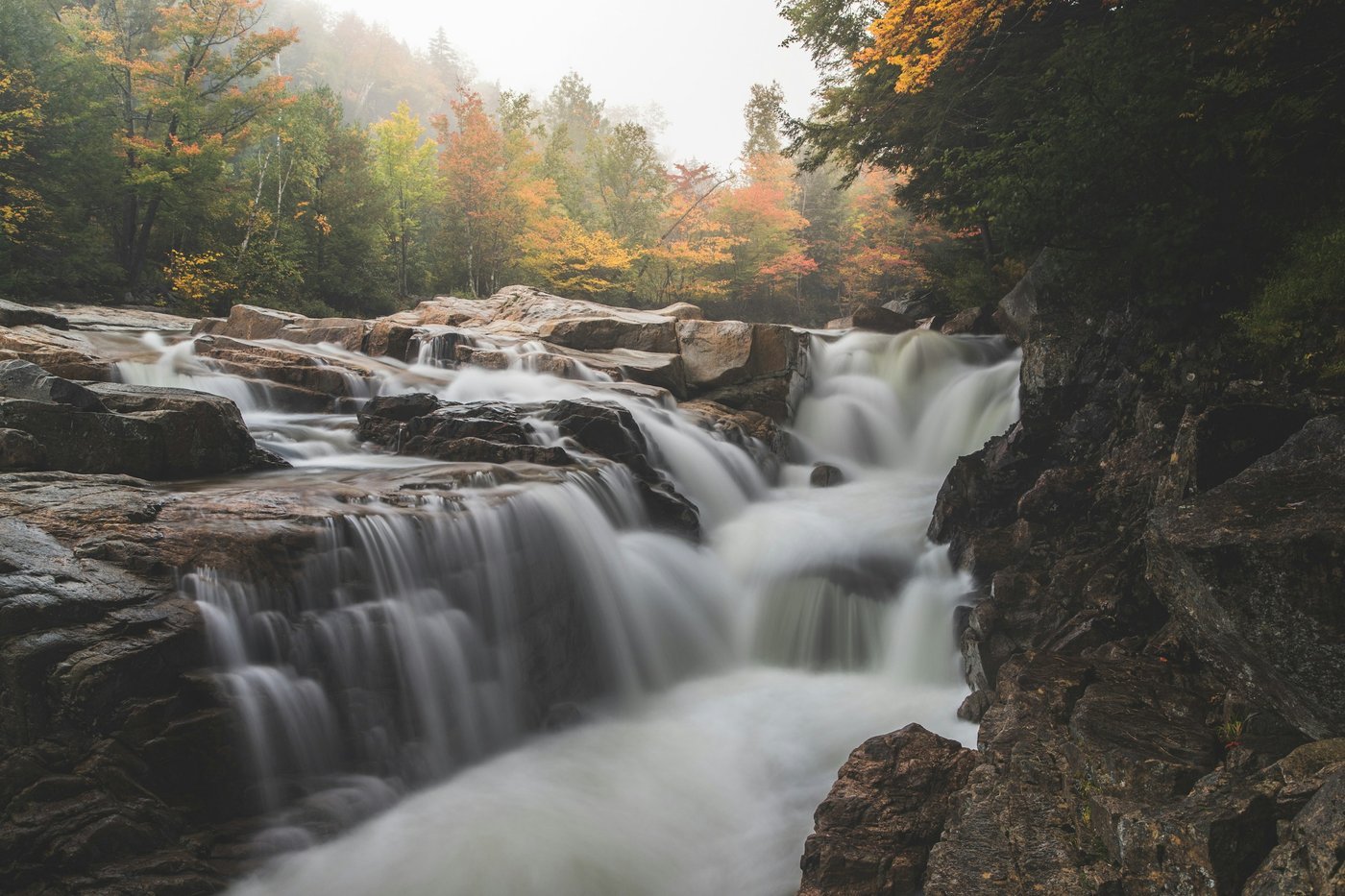 A long-exposure cascade over rocky ledges in a forest with early autumn colors (illustrative photo, not in Georgia).