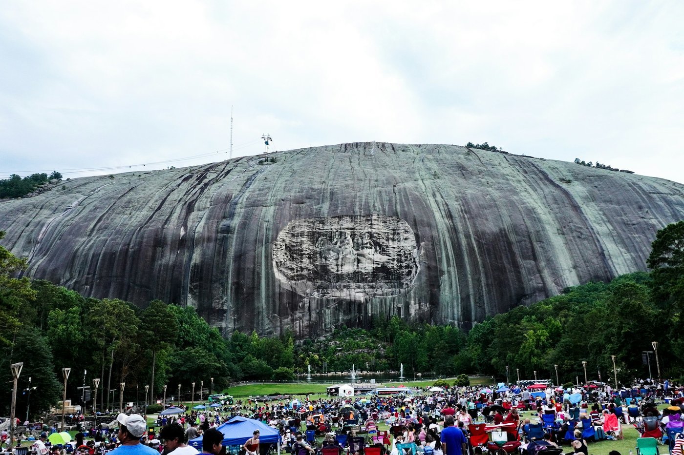 Stone Mountain's bare granite dome and carved face rising above forest, with a crowd on the lawn below.