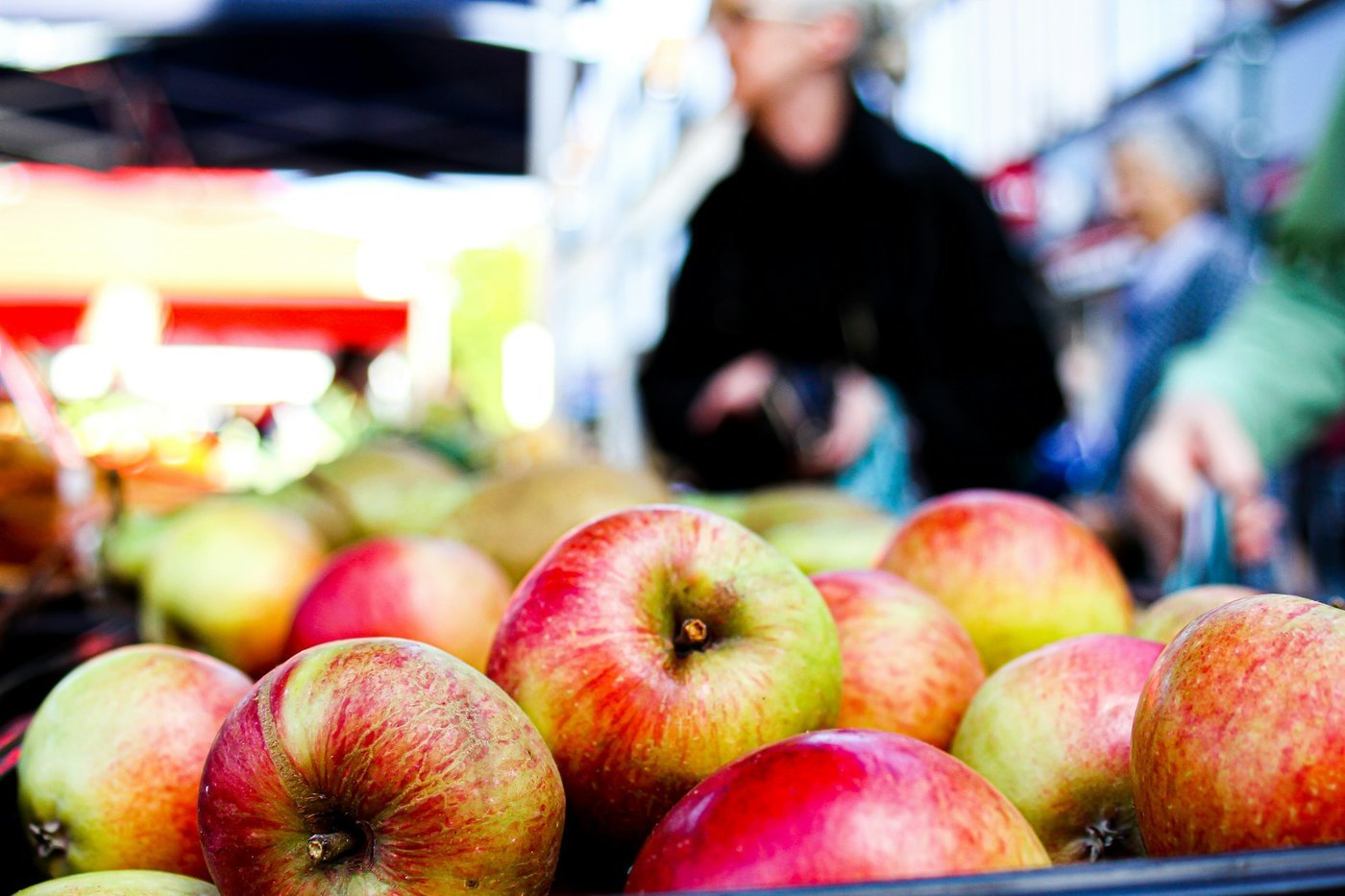 Red and green apples piled on a market stall with blurred shoppers behind (illustrative, not the Ellijay festival).