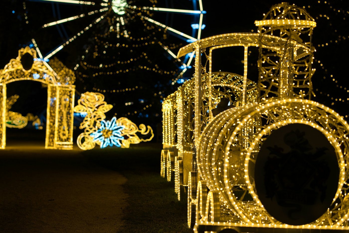 A train sculpture covered in warm string lights beside a lit Ferris wheel at night (illustrative holiday-lights photo, not a Georgia train).