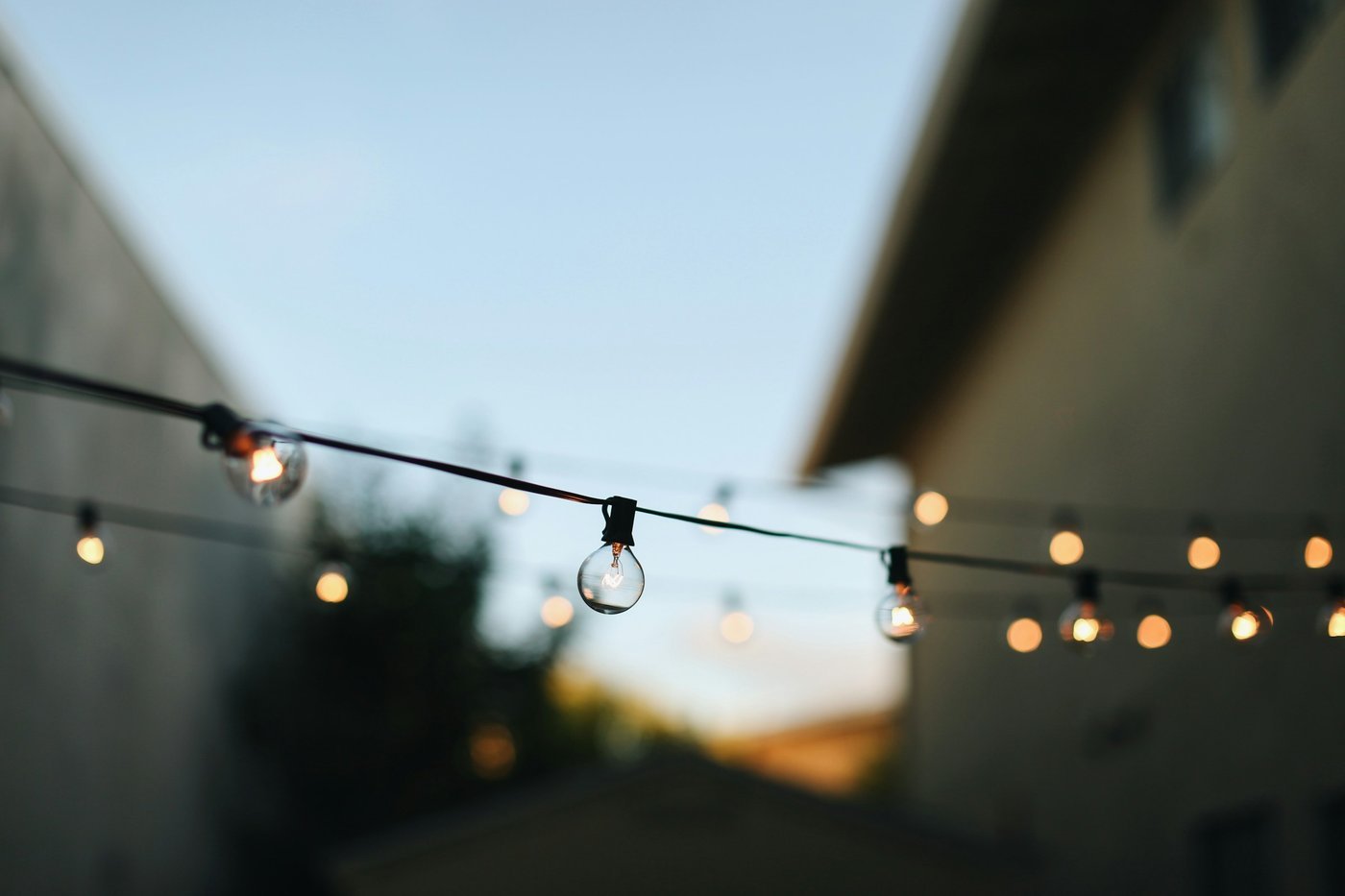 Strings of warm bulb lights hanging between buildings at dusk.