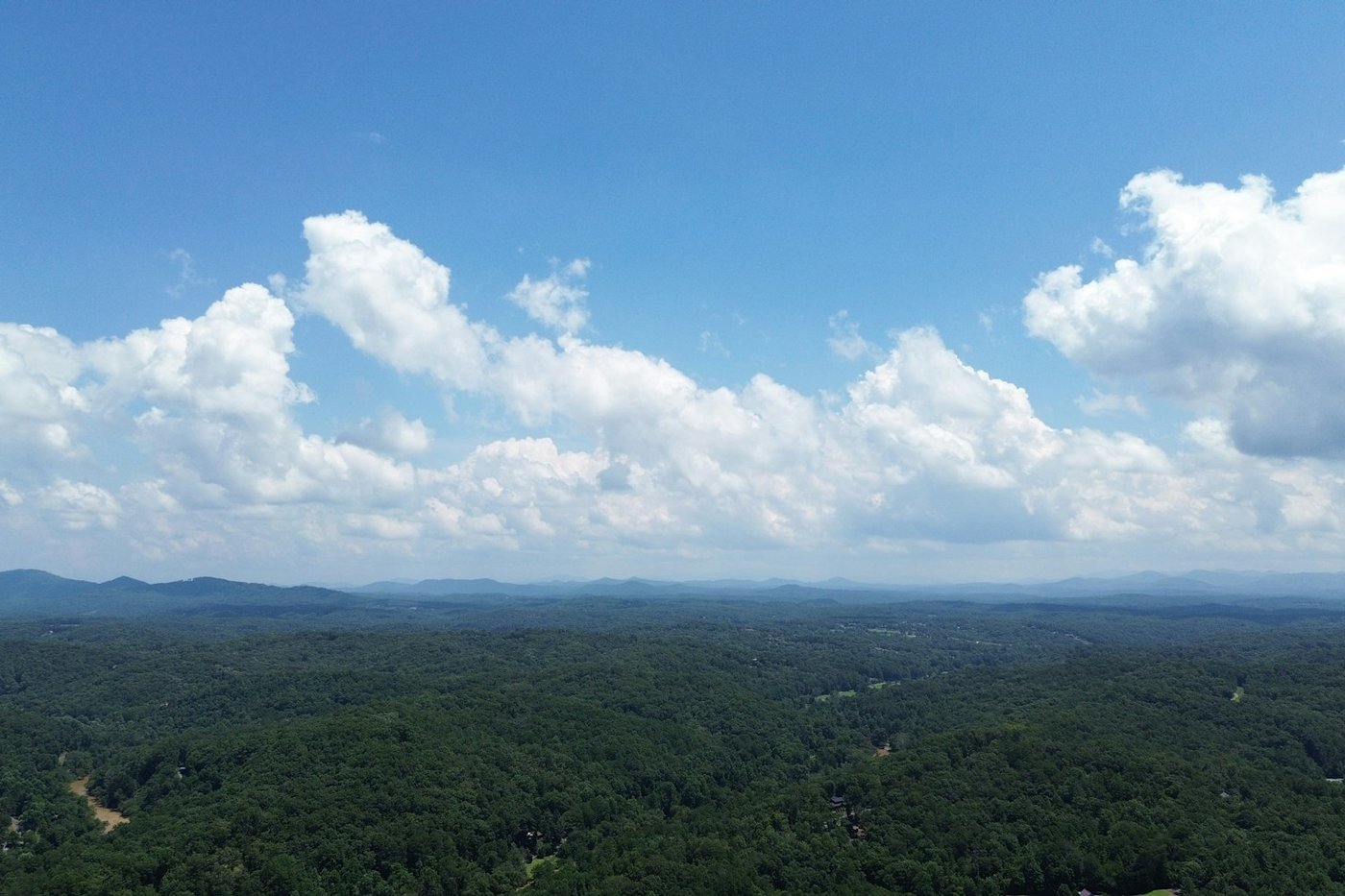 An aerial view of forested North Georgia mountains near Blue Ridge under a blue sky with clouds.