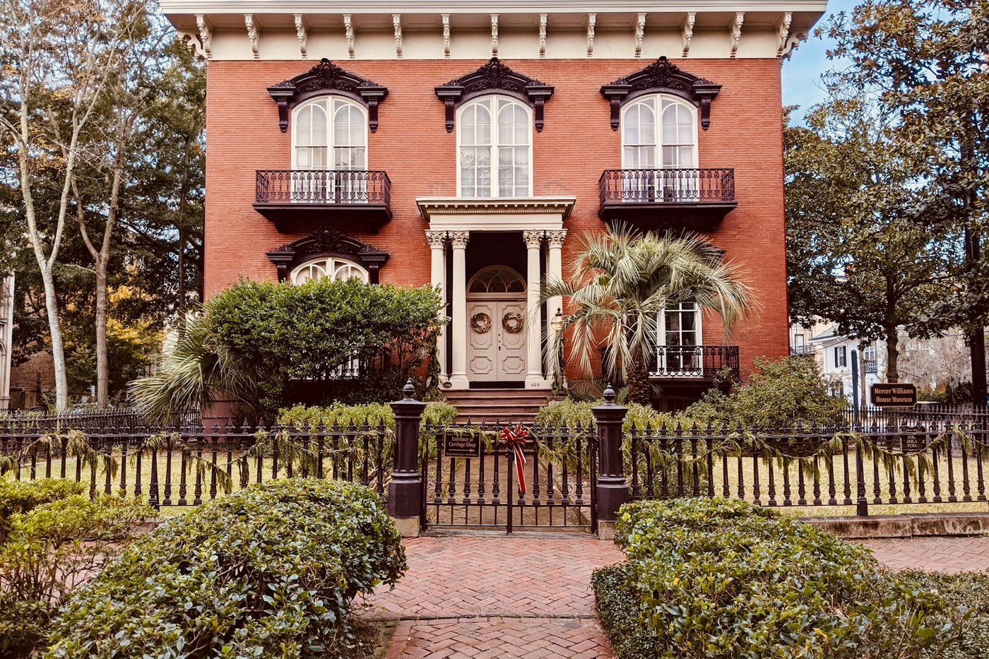 A red-brick historic mansion in Savannah, Georgia with wreaths on the door and garland on the fence.