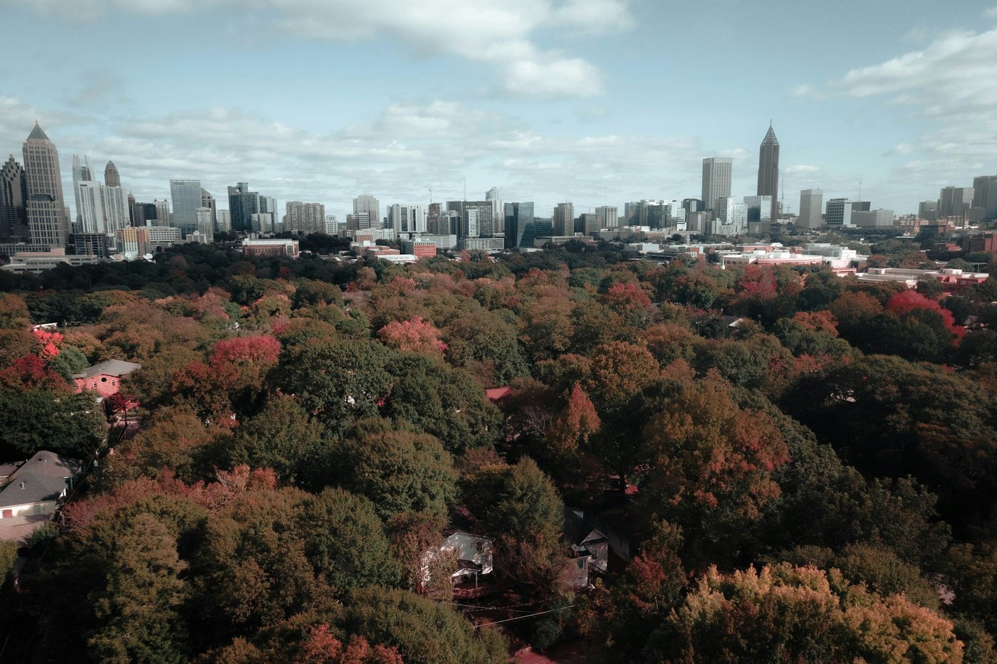 An aerial view of tree-covered Atlanta neighborhoods in autumn with the downtown skyline behind.