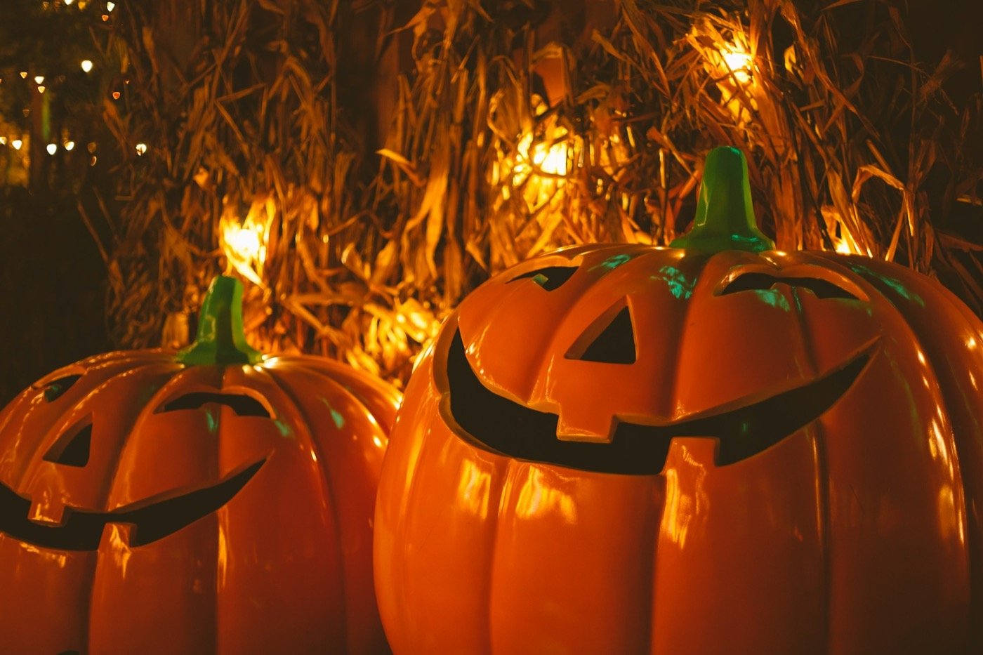 Two smiling jack-o'-lanterns glowing at night in front of straw bales and string lights