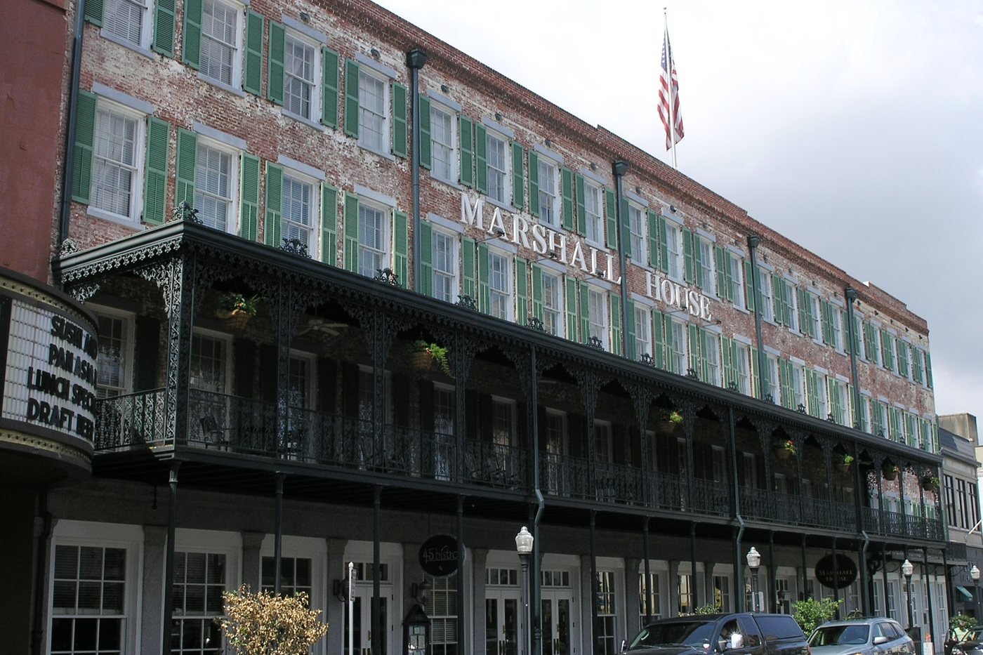 The four-story brick Marshall House on Broughton Street in Savannah, with green shutters and a long two-story cast-iron veranda