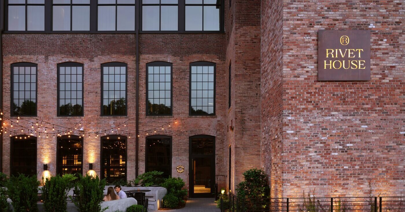 Rivet House's red-brick mill building at Southern Mill in Athens at dusk, with string lights over the patio and the Rivet House sign on the wall