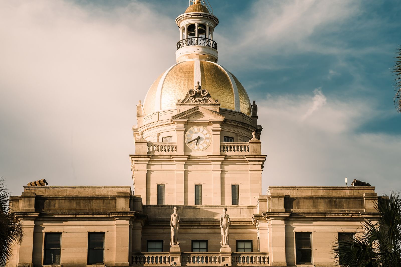 The gold dome and clock tower of Savannah City Hall against a blue sky