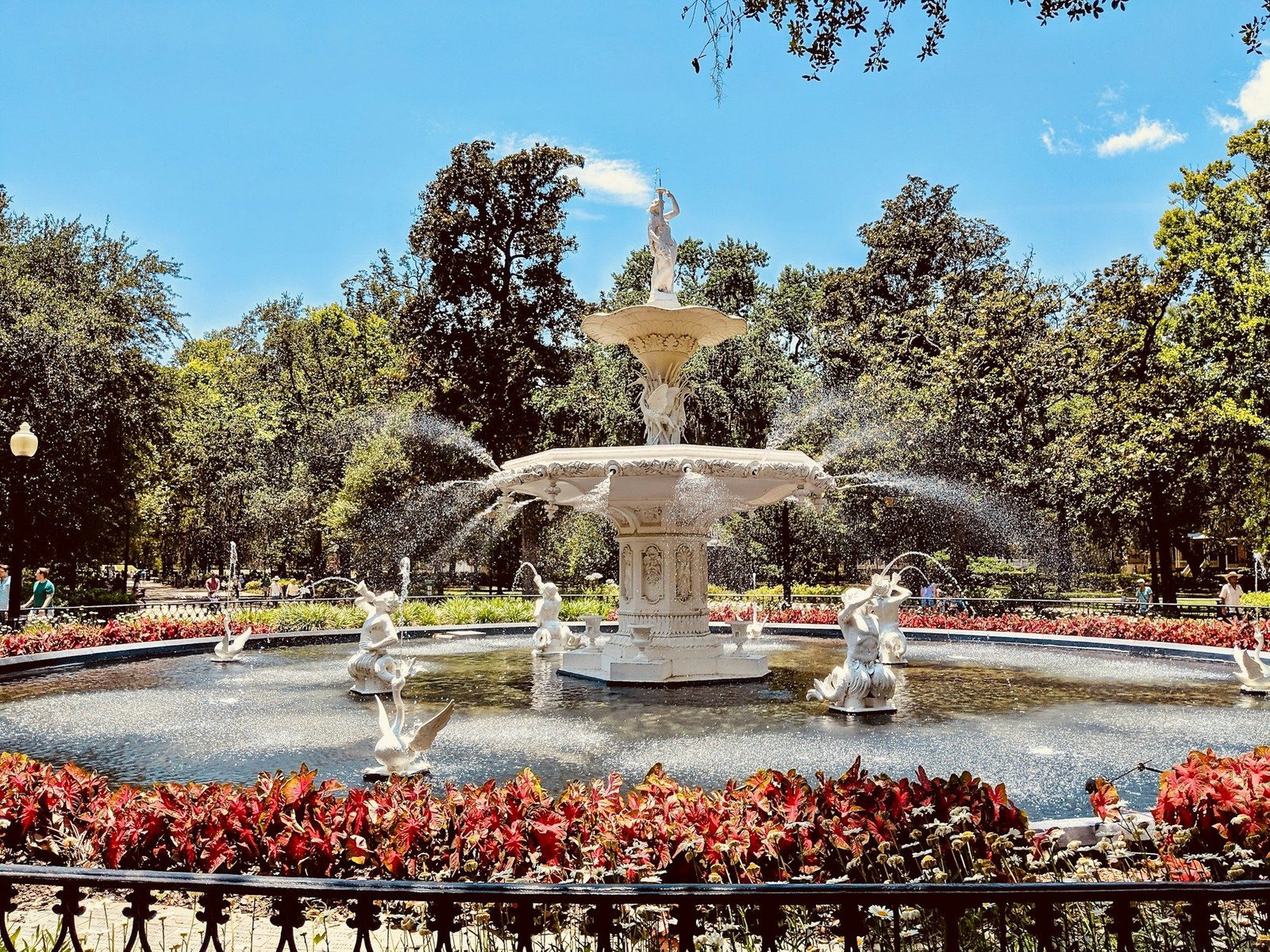 The white cast-iron fountain in Forsyth Park, Savannah, with red flowers in the foreground on a sunny day