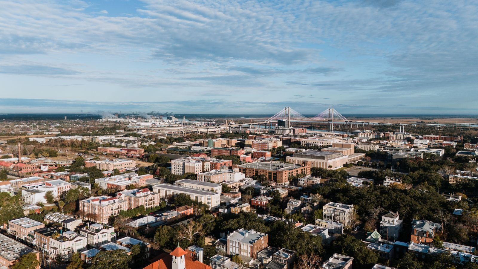Aerial view of Savannah's historic district rooftops and live oaks with the Talmadge Memorial Bridge on the horizon