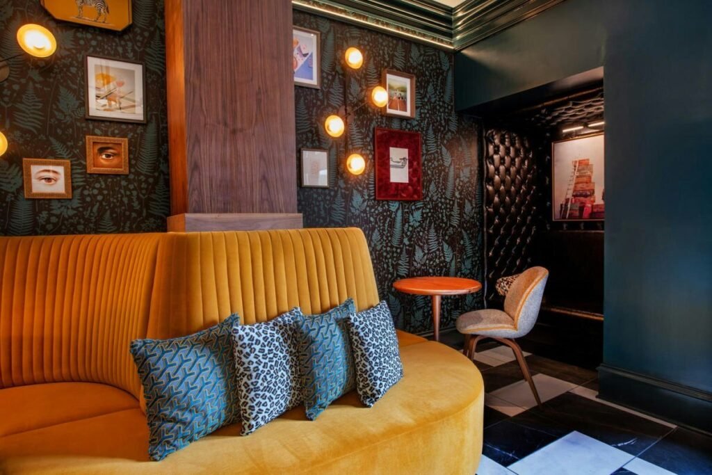 Lobby seating at The Bell Hotel in Athens: a curved mustard velvet banquette against dark patterned wallpaper hung with small framed art